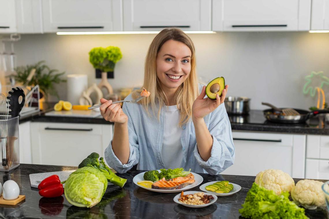 Bildnachweis: © stock.adobe.com / Andrii Iemelianenko Frau sitzt in der Küche und Fisch, frisches Gemüse und Nüsse